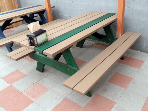 Green and gray Commercial quality eco Outdoor Attached Bench Picnic Table slanted right on a restaurant bar patio.
