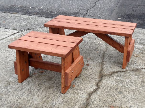 A short and a medium Commercial quality Outdoor Picnic Table Bench slanted slightly to the left on the sidewalk.