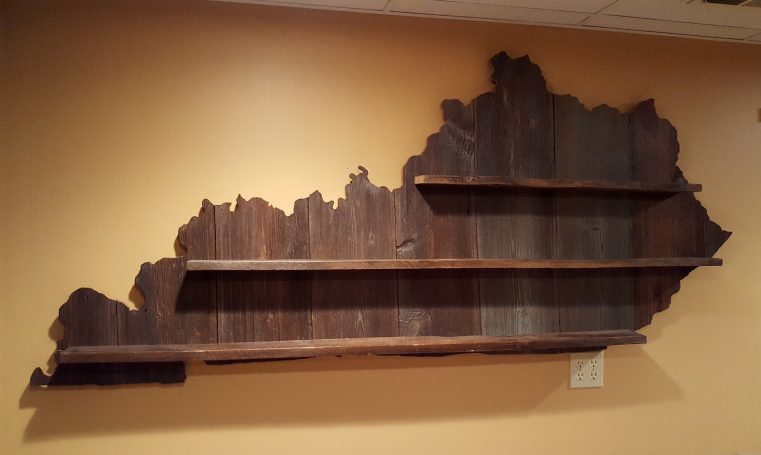 Handcrafted Barnwood Kentucky Derby Glass Shelf without glasses hanging slightly slanted to the right on a yellow wall.