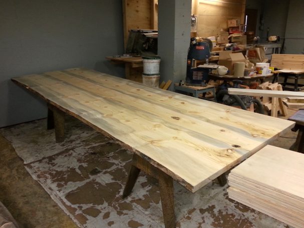 Finishing of Custom Live Edge Blue Pine Slab Conference Table Top in a woodworking shop.