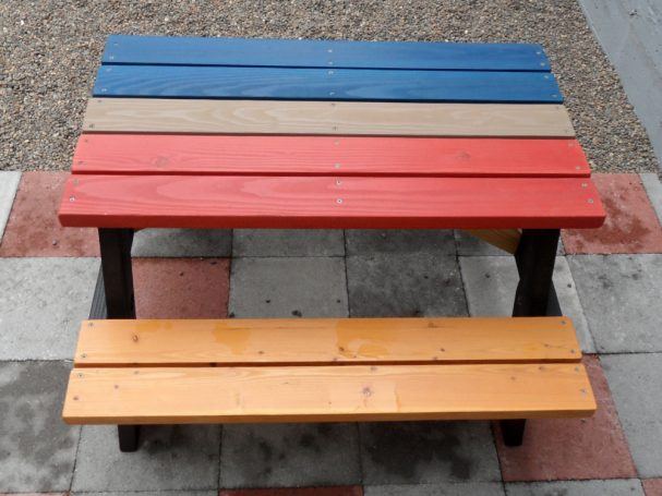 4' Multicolored Commercial quality Eco-friendly Outdoor Kids Attached Bench Picnic Table from the side on a sidewalk.