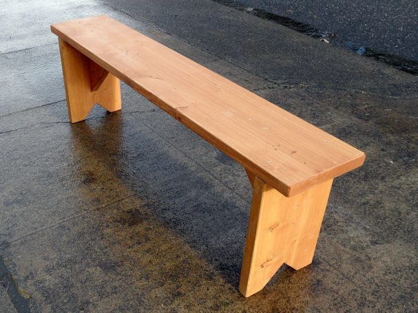 Large Commercial quality eco-friendly Outdoor Farmhouse Bench slanted to the left on a sidewalk.