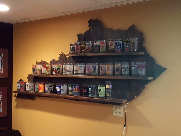 Handcrafted Barnwood Kentucky Derby Glass Shelf with glasses hanging slanted to the left on a wall. 