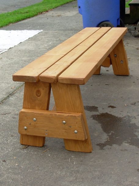 A large Commercial quality eco-friendly Outdoor Picnic Table Bench slanted to the right on the sidewalk.