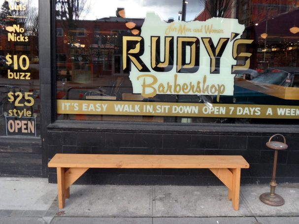 Commercial quality eco-friendly Outdoor Farmhouse Bench on the sidewalk outside a barbershop.