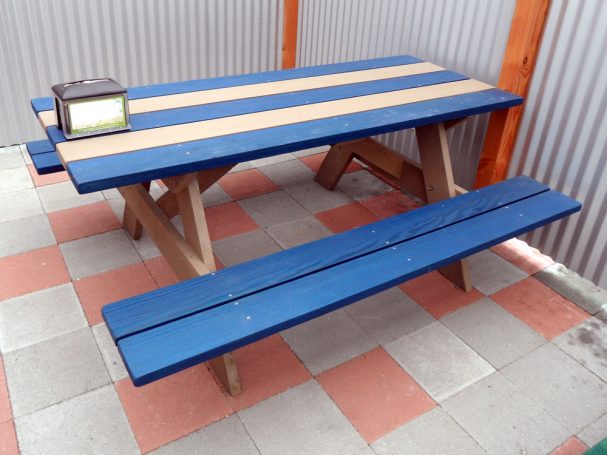 Striped blue and gray Commercial quality eco Outdoor Attached Bench Picnic Table slanted right on restaurant bar patio.