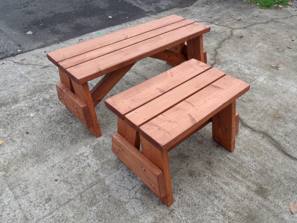 A short and a medium Commercial quality eco-friendly Outdoor Picnic Table Bench slanted to the right on the sidewalk.