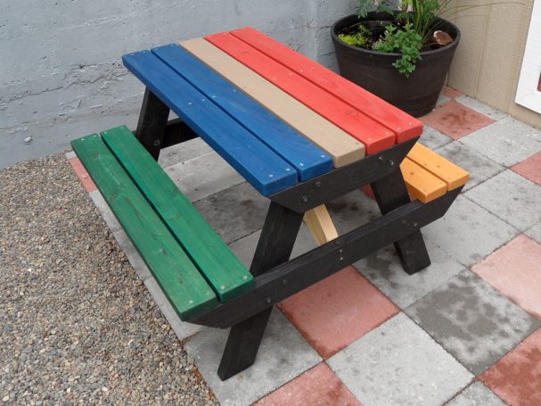 Multicolored Commercial quality Eco-friendly Outdoor Kids Attached Bench Picnic Table slanted to the left on a sidewalk.
