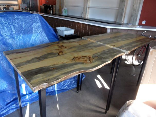 Two commercial quality Blue Pine Live Edge Slab Table Top dining tables slanted to the right at a restaurant bar.