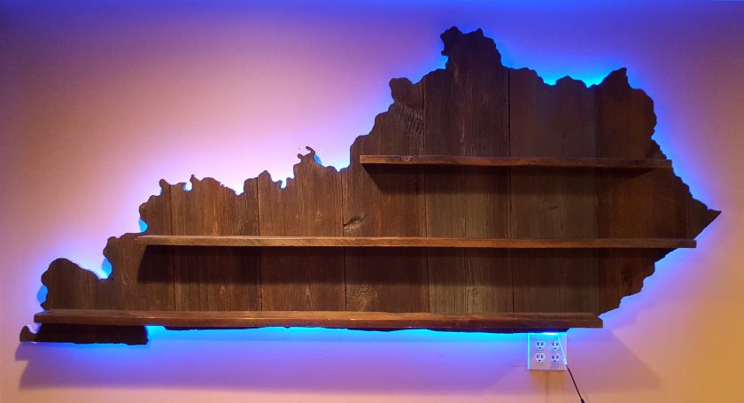 Backlit Handcrafted Barnwood Kentucky Derby Glass Shelf without glasses hanging flat on a yellow wall.