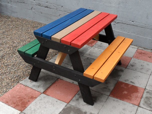 4' Multicolored Commercial quality Eco-friendly Outdoor Kids Attached Bench Picnic Table slanted to the right on a sidewalk.