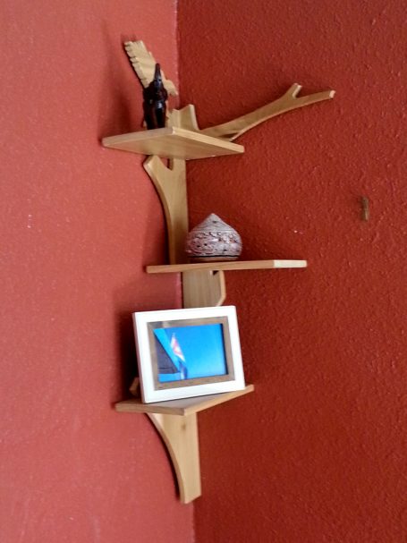 Handcrafted Poplar Bird and Tree Corner Shelf hanging in the corner on a red wall slanted to the right.