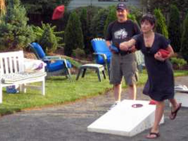 Two people playing in a cornhole tournament on back-to-back sturdy high quality solid box design Cornhole Board Sets.