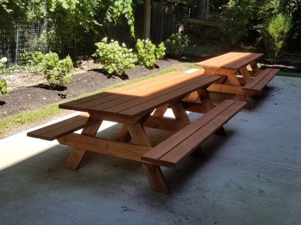 Two Large Commercial quality eco-friendly Outdoor Attached Bench Picnic Tables slanted to the right on a patio.