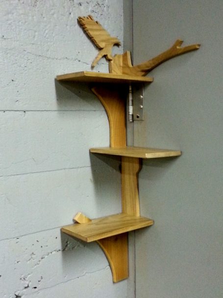 Handcrafted Poplar Bird and Tree Corner Shelf hanging in the corner slanted to the left.