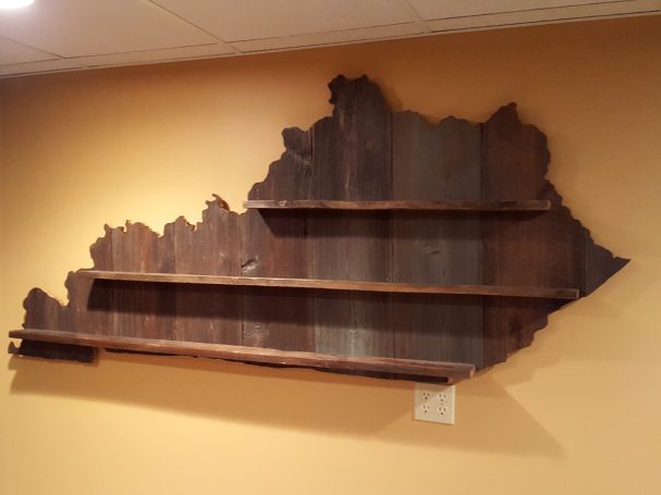 Handcrafted Barnwood Kentucky Derby Glass Shelf without glasses hanging slightly slanted to the left on a yellow wall. 