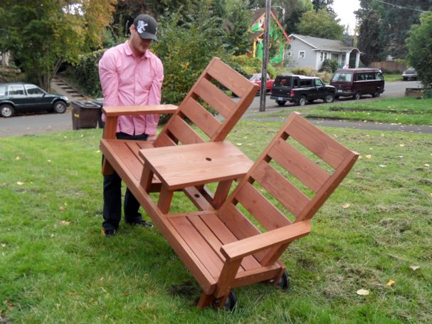 A man moving a Custom 5' Commercial quality eco-friendly Outdoor Park Bench with center table and wheels.