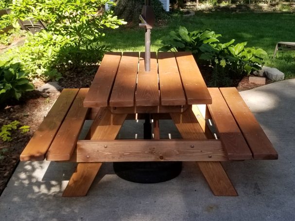 Commercial quality eco-friendly Outdoor Attached Bench Picnic Table with an umbrella from the front on a patio.