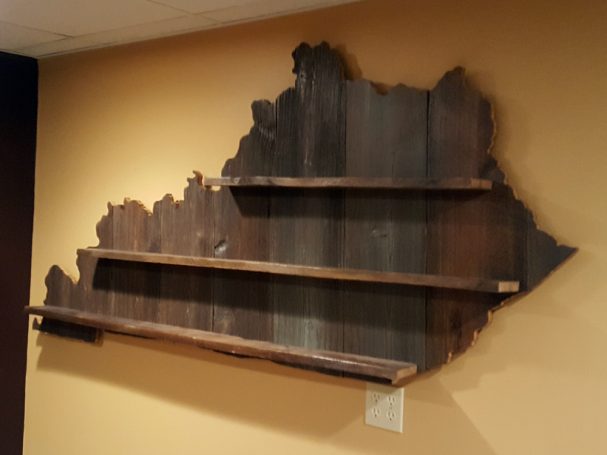 Handcrafted Barnwood Kentucky Derby Glass Shelf without glasses hanging slanted to the left on a yellow wall. 