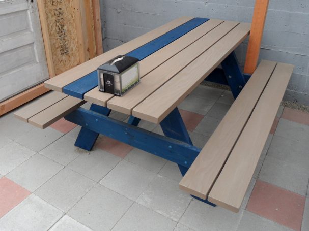 Blue and gray Commercial quality eco Outdoor Attached Bench Picnic Table slanted right on a restaurant bar patio.