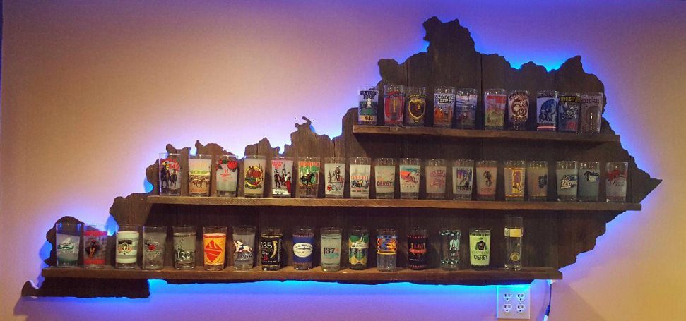 Backlit blue Handcrafted Barnwood Kentucky Derby Glass Shelf with glasses hanging flat on a yellow wall.