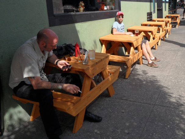 People at small Commercial quality eco-friendly Outdoor Attached Bench Picnic Tables in a row at a restaurant bar.