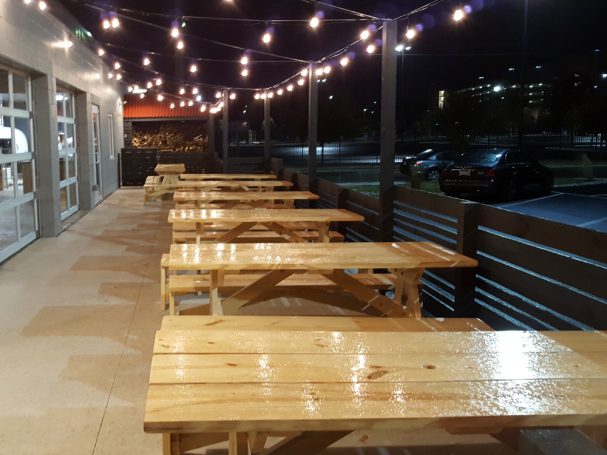 Commercial quality eco-friendly Outdoor Attached Bench Picnic Tables from the side on a rainy patio at a restaurant bar.