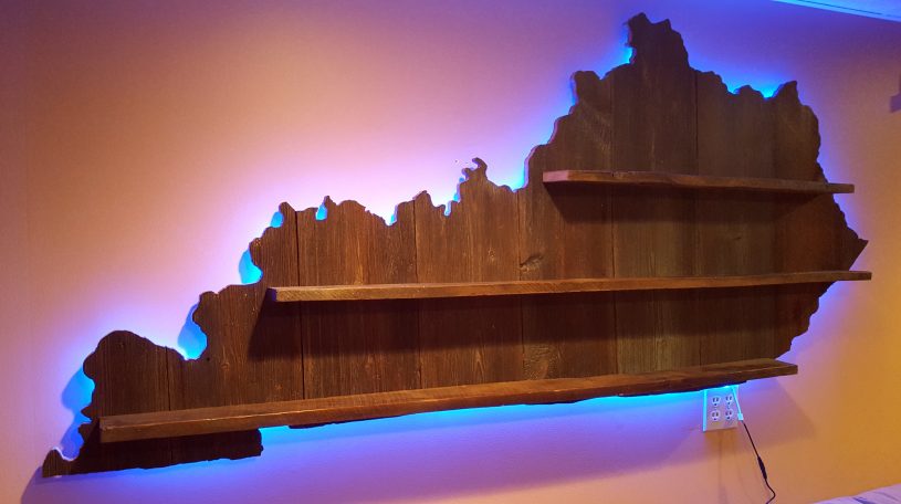 Backlit Handcrafted Barnwood Kentucky Derby Glass Shelf without glasses hanging slanted to the right on a yellow wall.